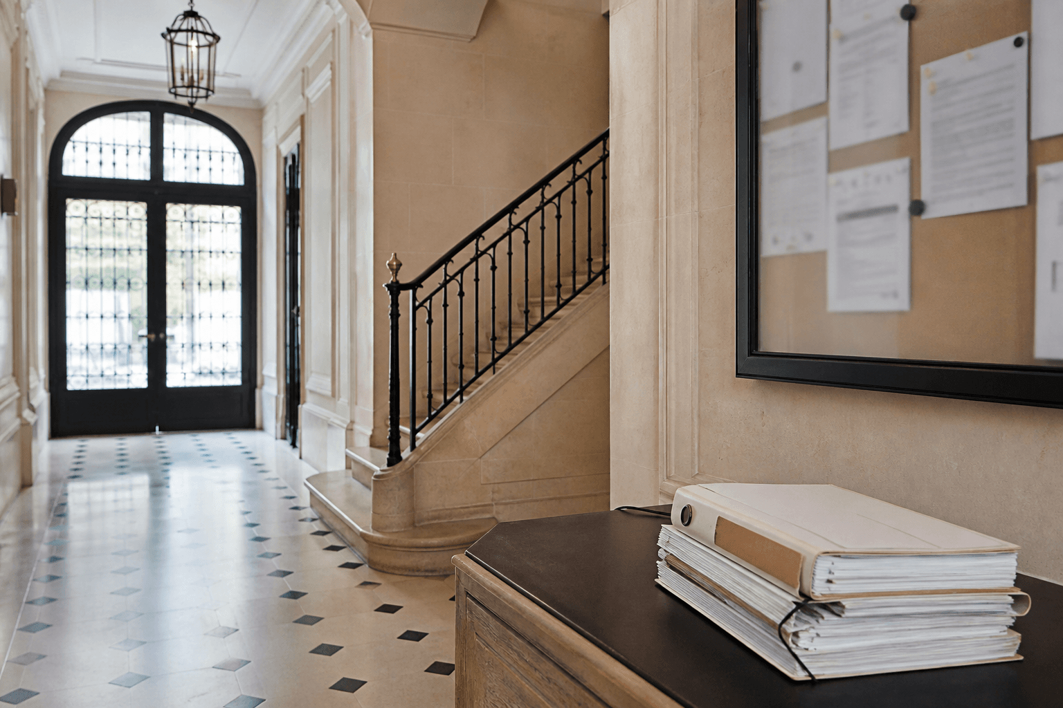 Hall d’immeuble parisien avec dossier de copropriété posé près d’un tableau d’affichage flouté
